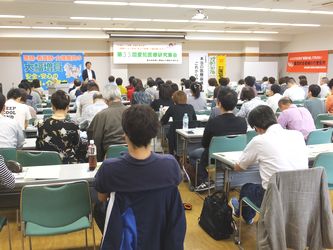 【写真　記念講演は会場いっぱいの参加者で熱気】